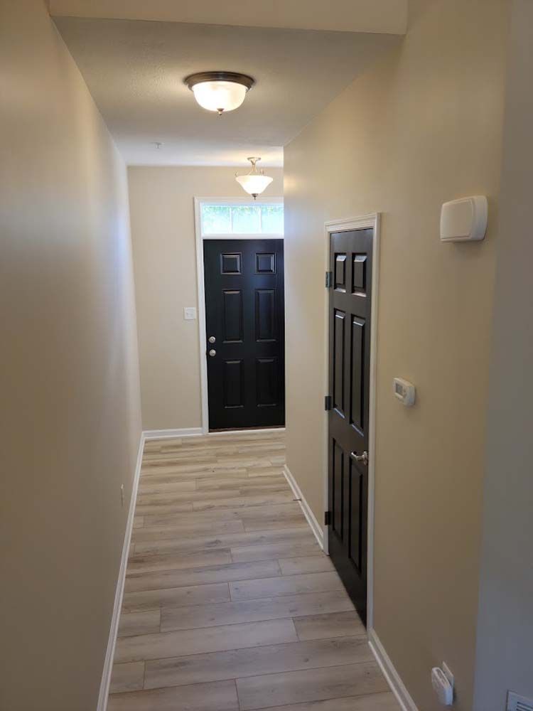 A hallway with a black door and a light on the ceiling.