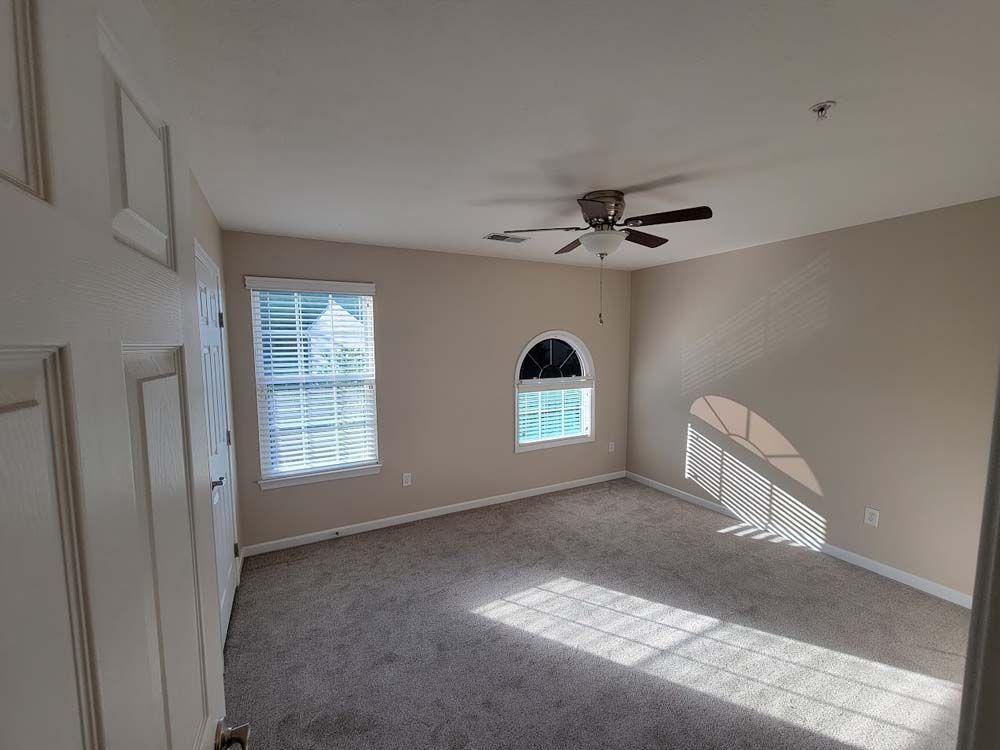 An empty bedroom with a ceiling fan and two windows.