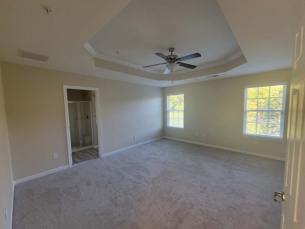 An empty bedroom with a ceiling fan and two windows.