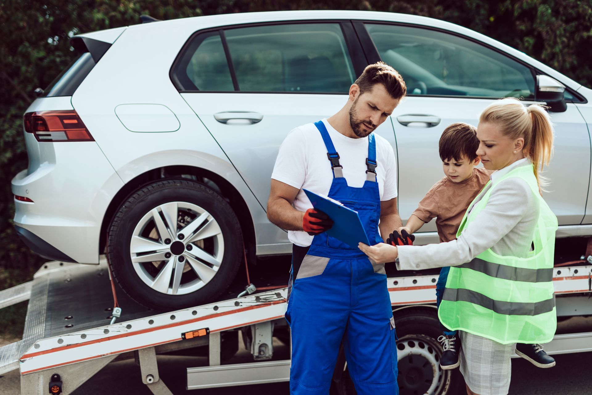 A man and a woman are standing next to a tow truck with a car on it.