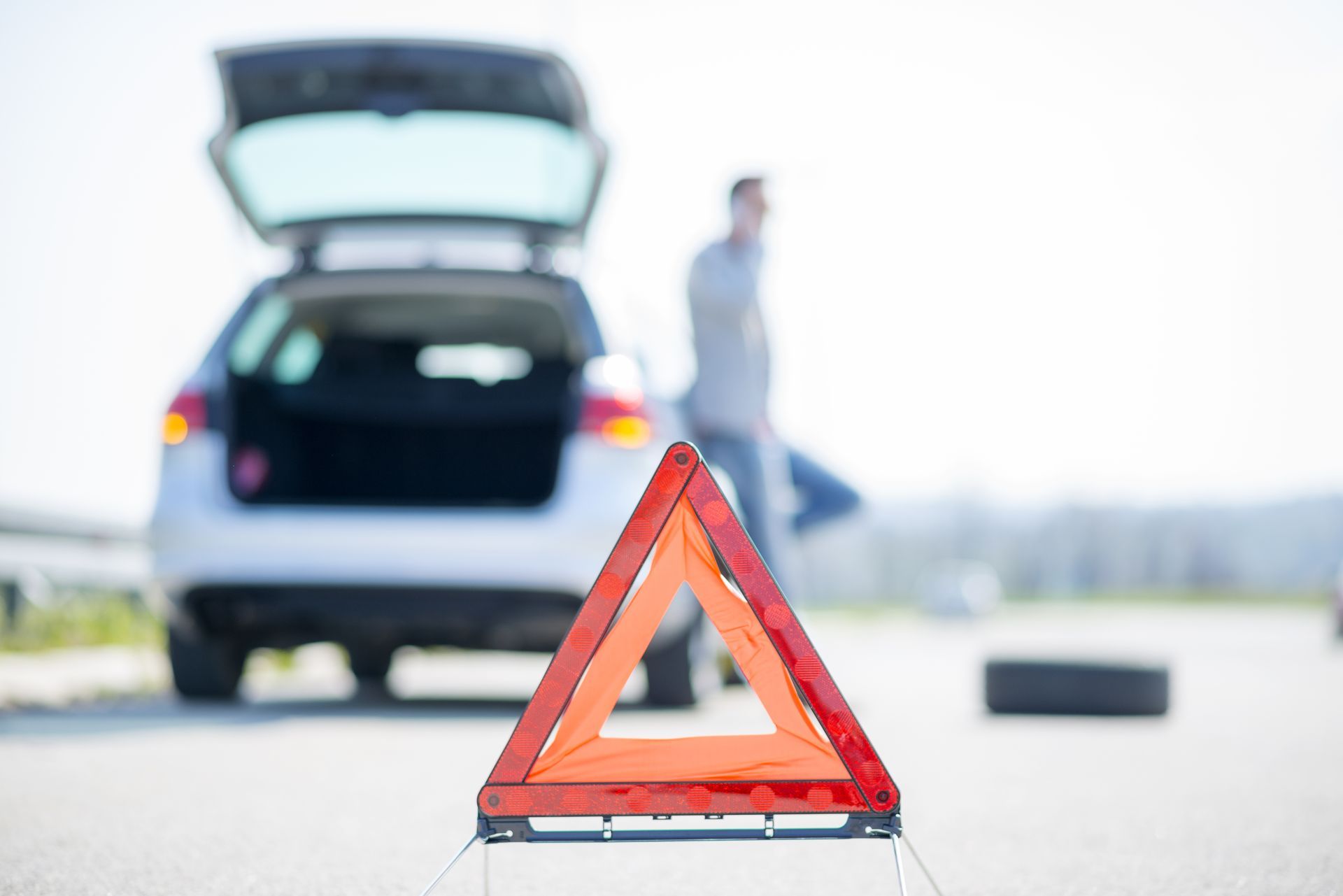 A man is changing a tire on the side of the road next to a warning triangle.