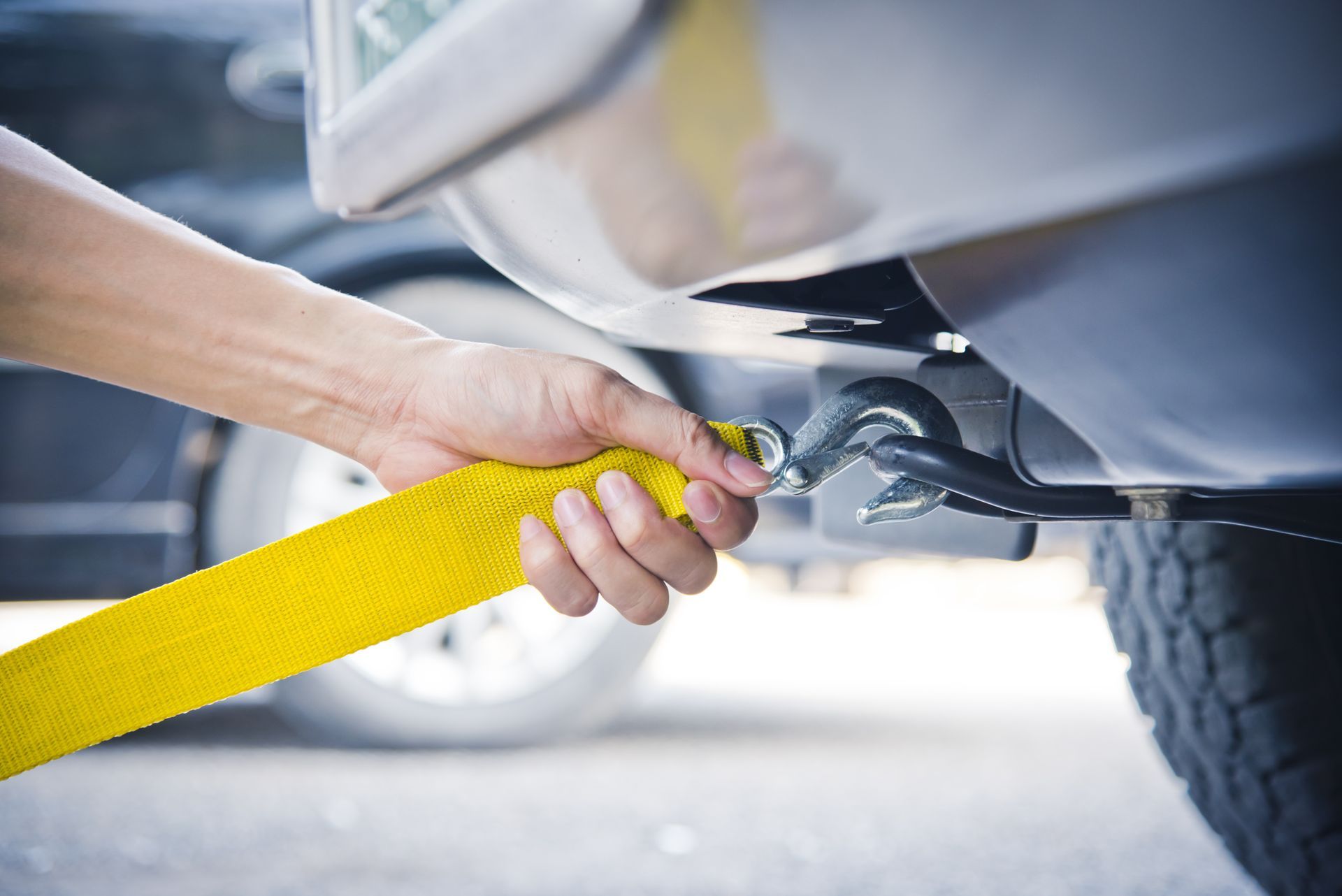 A person is attaching a yellow tow strap to a car.