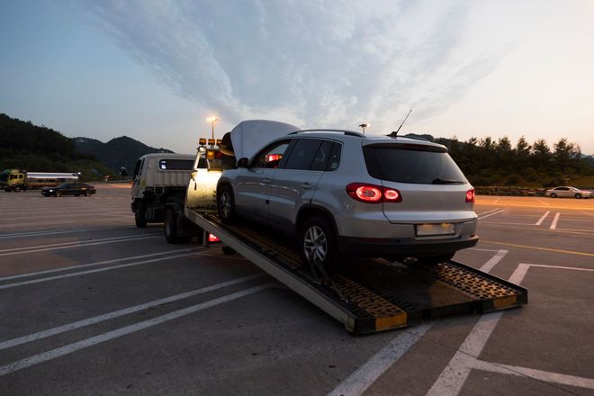 A car is being towed by a tow truck in a parking lot.