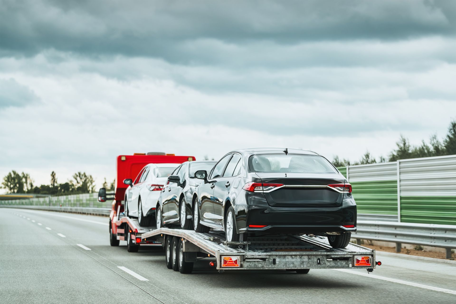 A tow truck is carrying two cars on a highway.