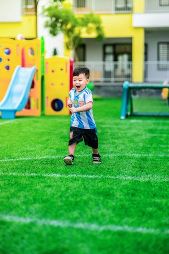 Child standing on a green playground lawn with slides and play equipment in the background