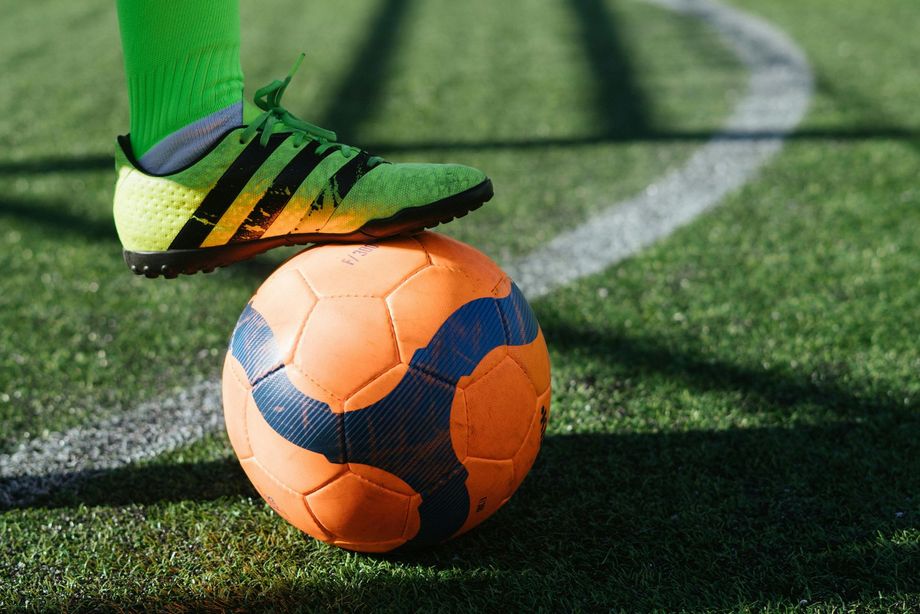 Soccer ball on grass field with a player’s green cleat pressing on top