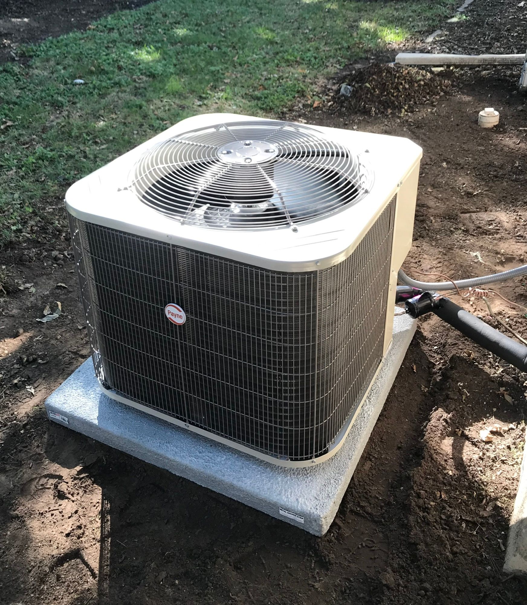 A large air conditioner is sitting on top of a concrete platform in the dirt.
