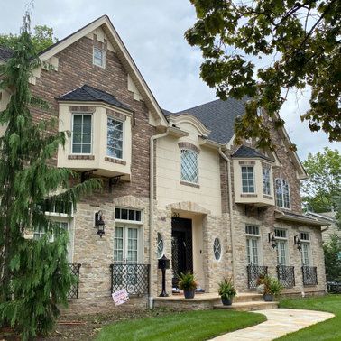 A large brick house with a black roof is sitting on top of a lush green lawn.