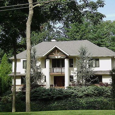 A large white house with a gray roof is surrounded by trees