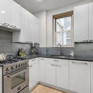A kitchen with white cabinets , a stove , a sink , and a window.