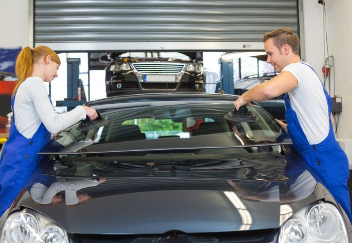A man and a woman are working on a car windshield in a garage.
