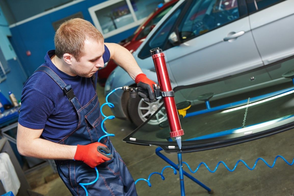A man is fixing a windshield on a car in a garage.