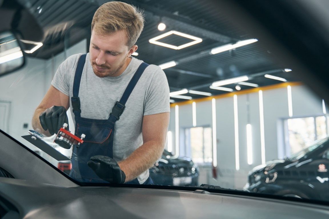 A man is fixing a windshield on a car in a garage.