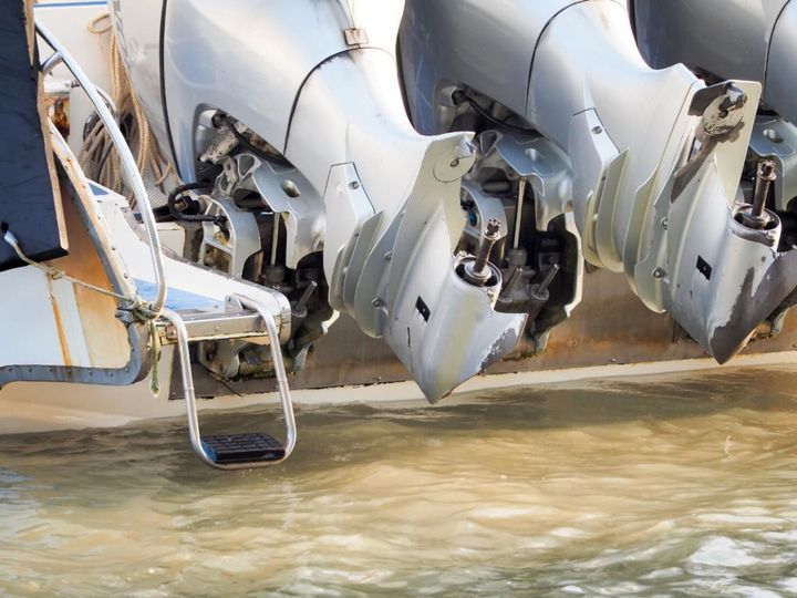 Three silver outboard boat motors with a boarding ladder in the water.