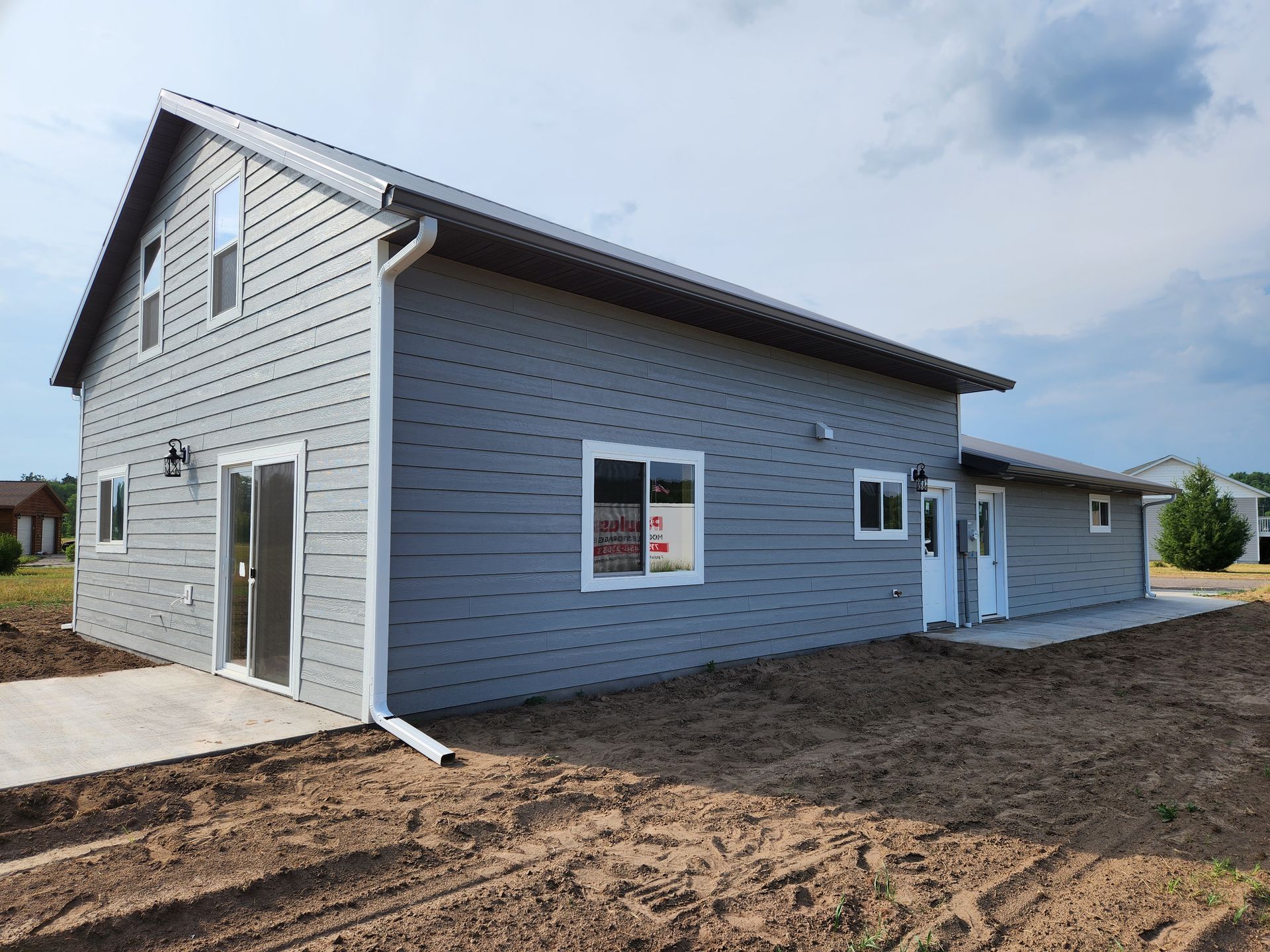 A gray house with a black roof is sitting in the middle of a dirt field.