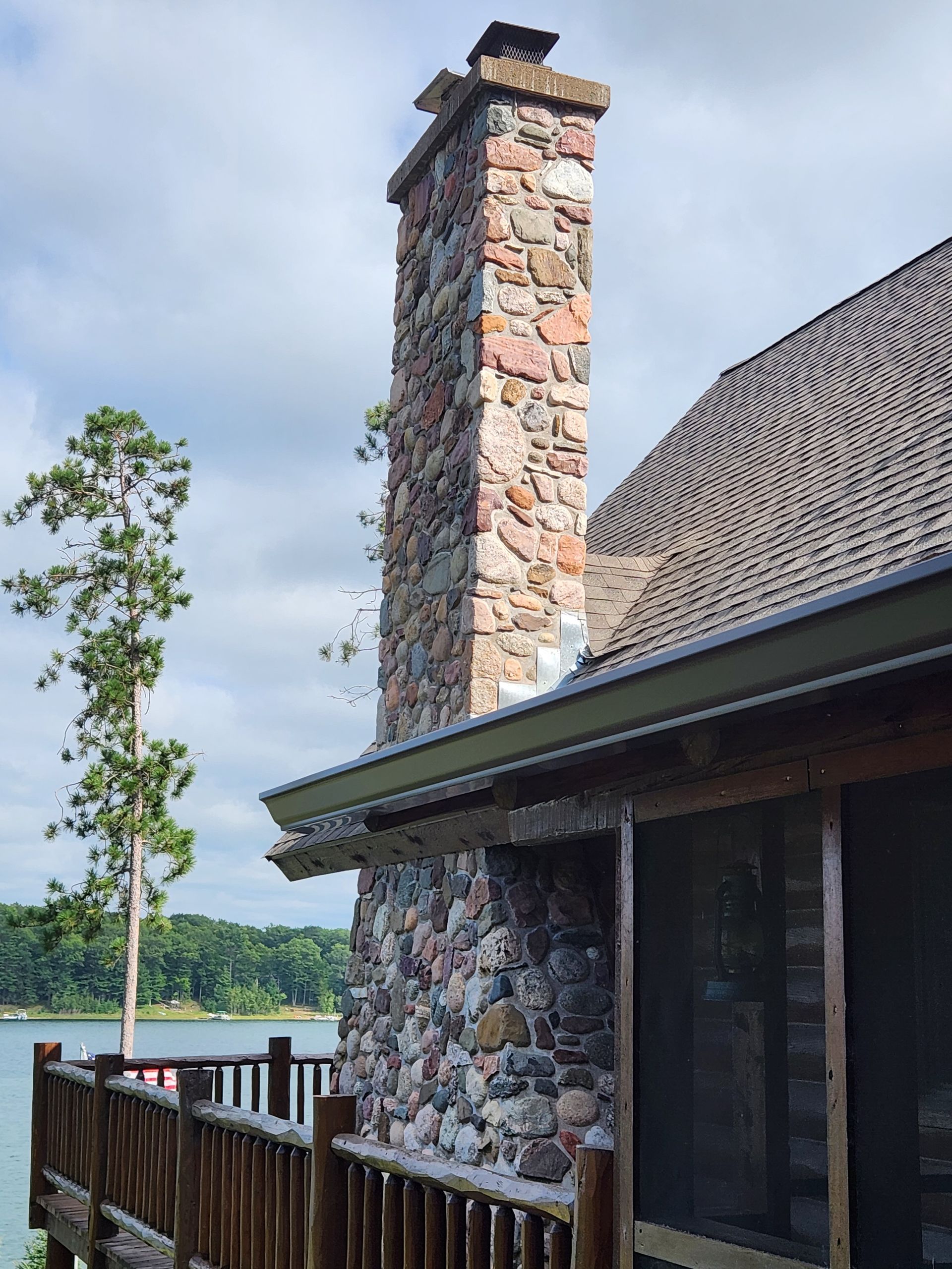 A stone chimney on the side of a house overlooking a lake