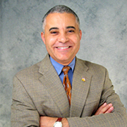 A man in a suit and tie is smiling with his arms crossed