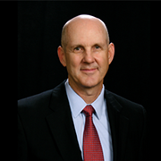 A bald man in a suit and tie is smiling for the camera.