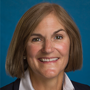 A woman with short brown hair is smiling in front of a blue background.