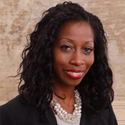 A woman wearing a pearl necklace and a black jacket is smiling for the camera.