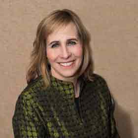 A woman in a green jacket is smiling for the camera.