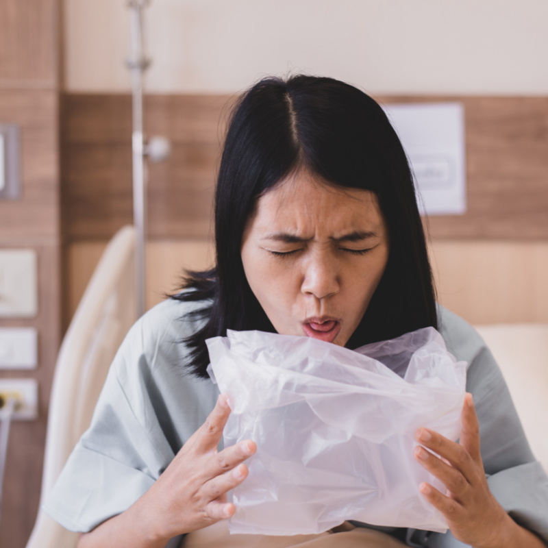 A person receiving an IV infusion at home. A medical professional assists while smiling near a window.