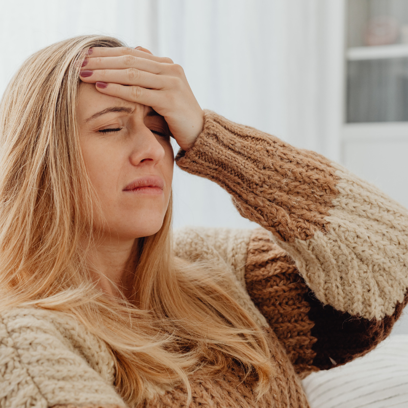 Woman with closed eyes holding her forehead, appearing to have a headache, wearing a patterned brown sweater.