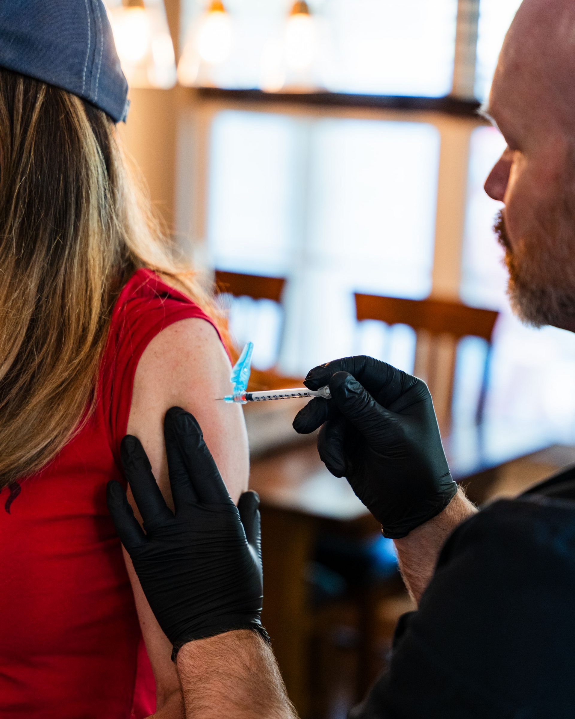 Person receiving a shot in their upper arm by a person wearing gloves. Interior setting.