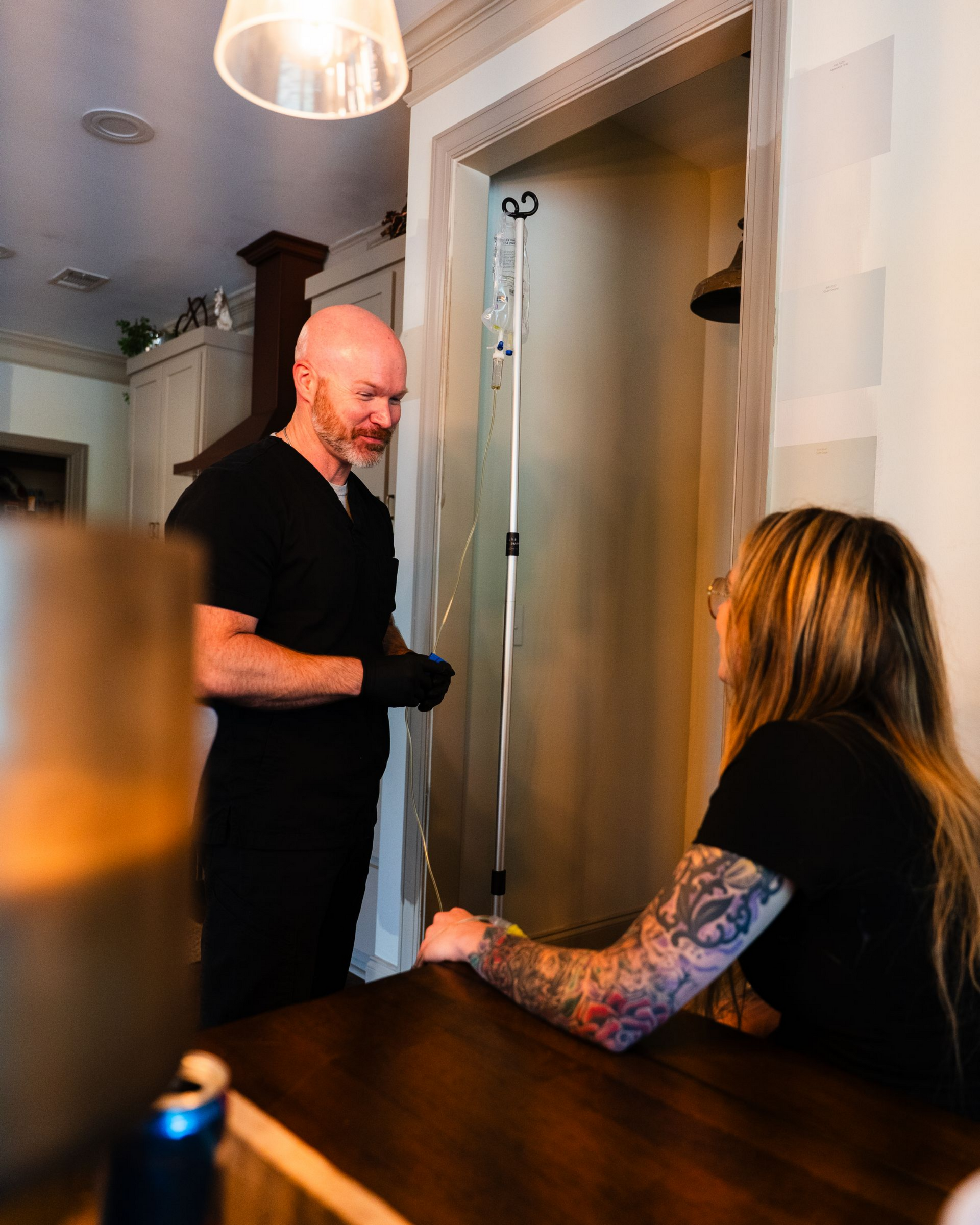 A medical professional speaks with a patient, an IV drip bag and stand are nearby.