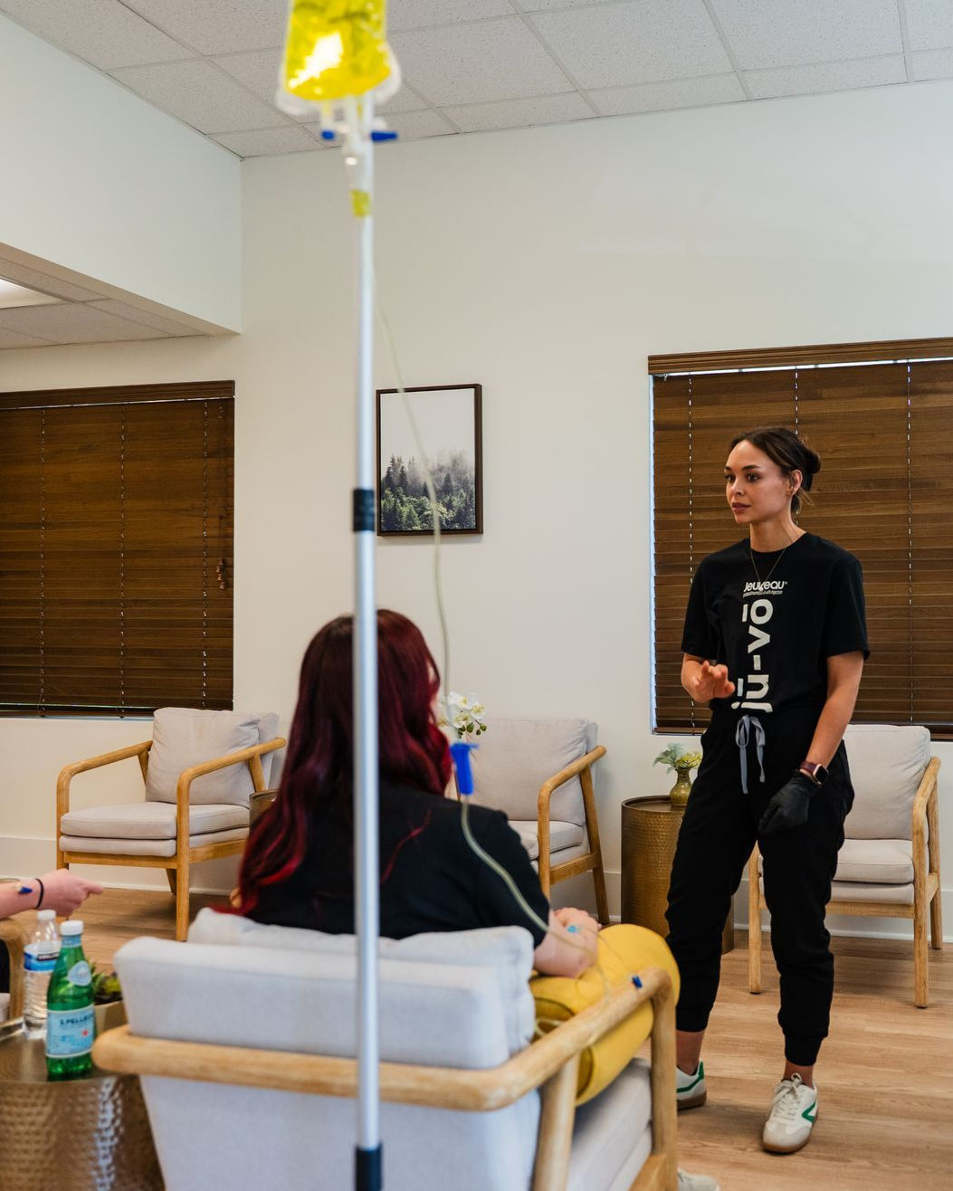 A person receives IV treatment in a clinic setting, while a staff member explains the procedure.