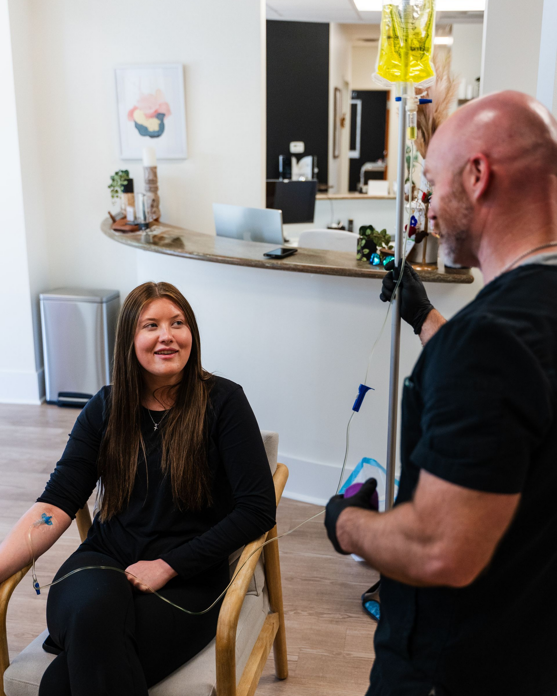 Woman receiving IV drip therapy while talking to a medical professional. White interior.