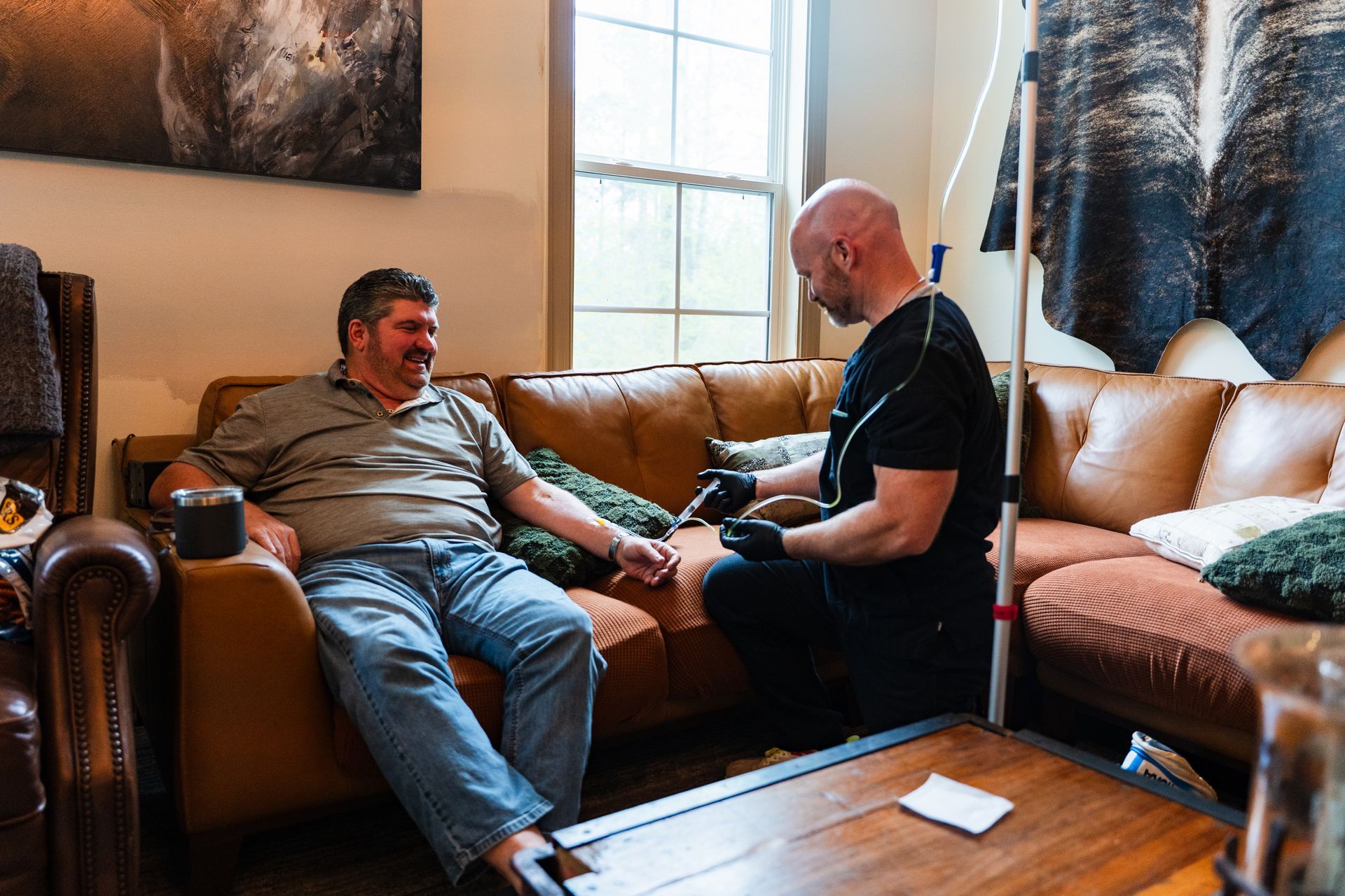 Man on couch receiving IV treatment at home from a health worker.