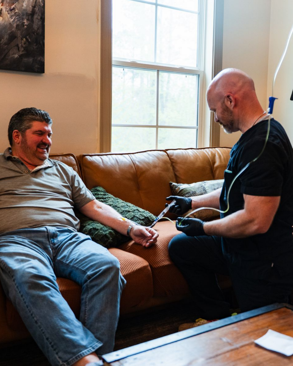 Man receiving IV drip on couch; healthcare worker preparing to insert the needle.