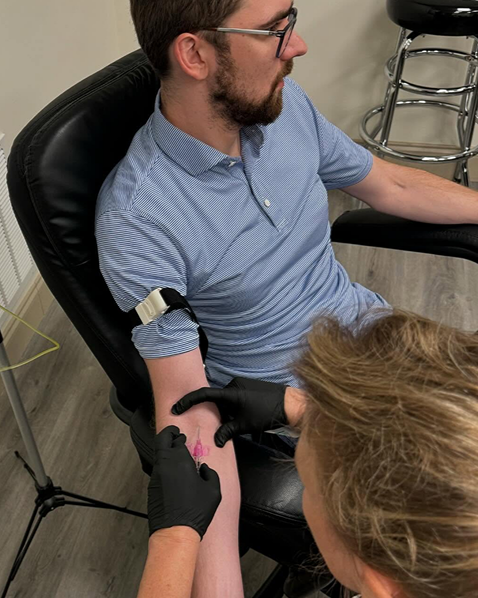 Person receiving a medical procedure, arm with tourniquet, healthcare worker prepping the arm for an injection.