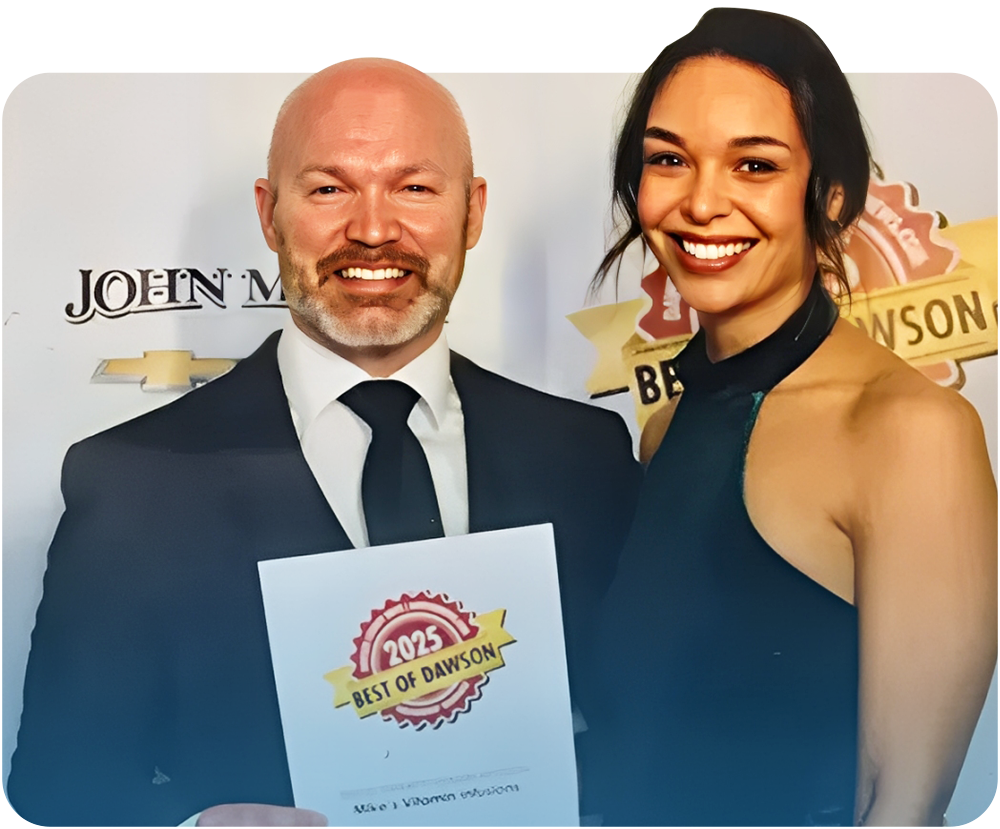 A man and woman smiling, holding an award. The man is bald, and they are in formal attire.