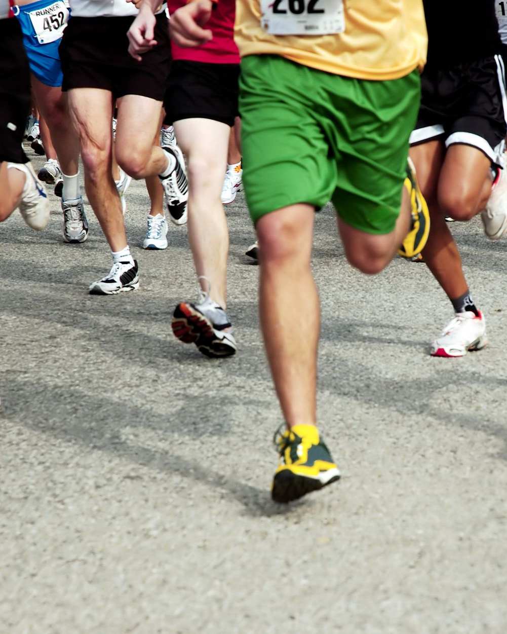 Runners in a race, close-up of legs. Asphalt road. Green, black, and white shorts. Yellow bibs and shoes.