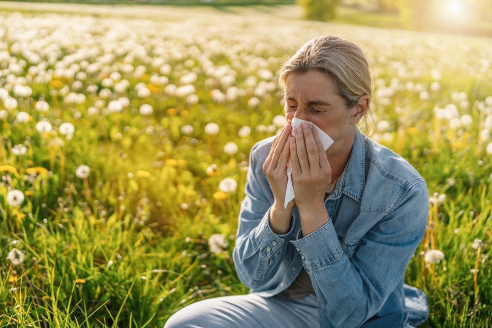 A woman is blowing her nose in a field of dandelions.