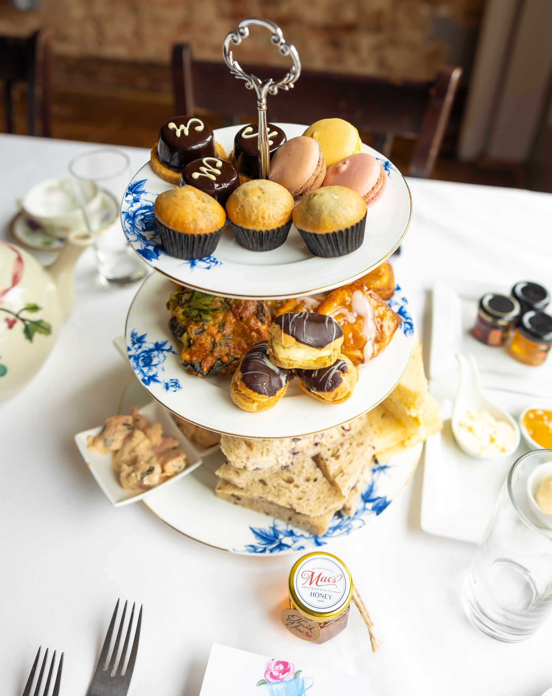 A three tiered cake stand filled with cupcakes and sandwiches on a table.