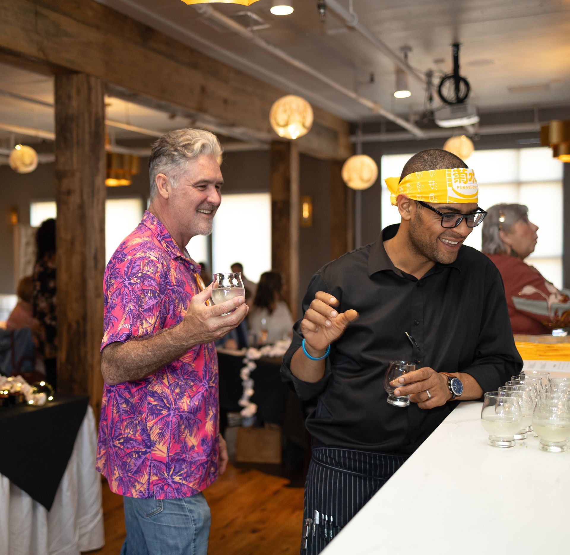 Two men are standing next to each other in a room holding drinks