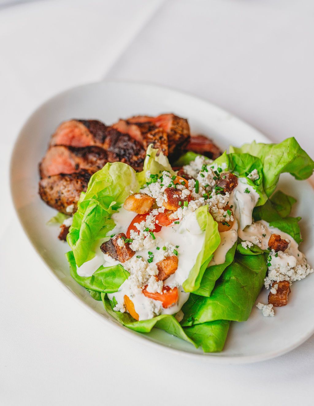 A white plate topped with a salad and meat on a table.