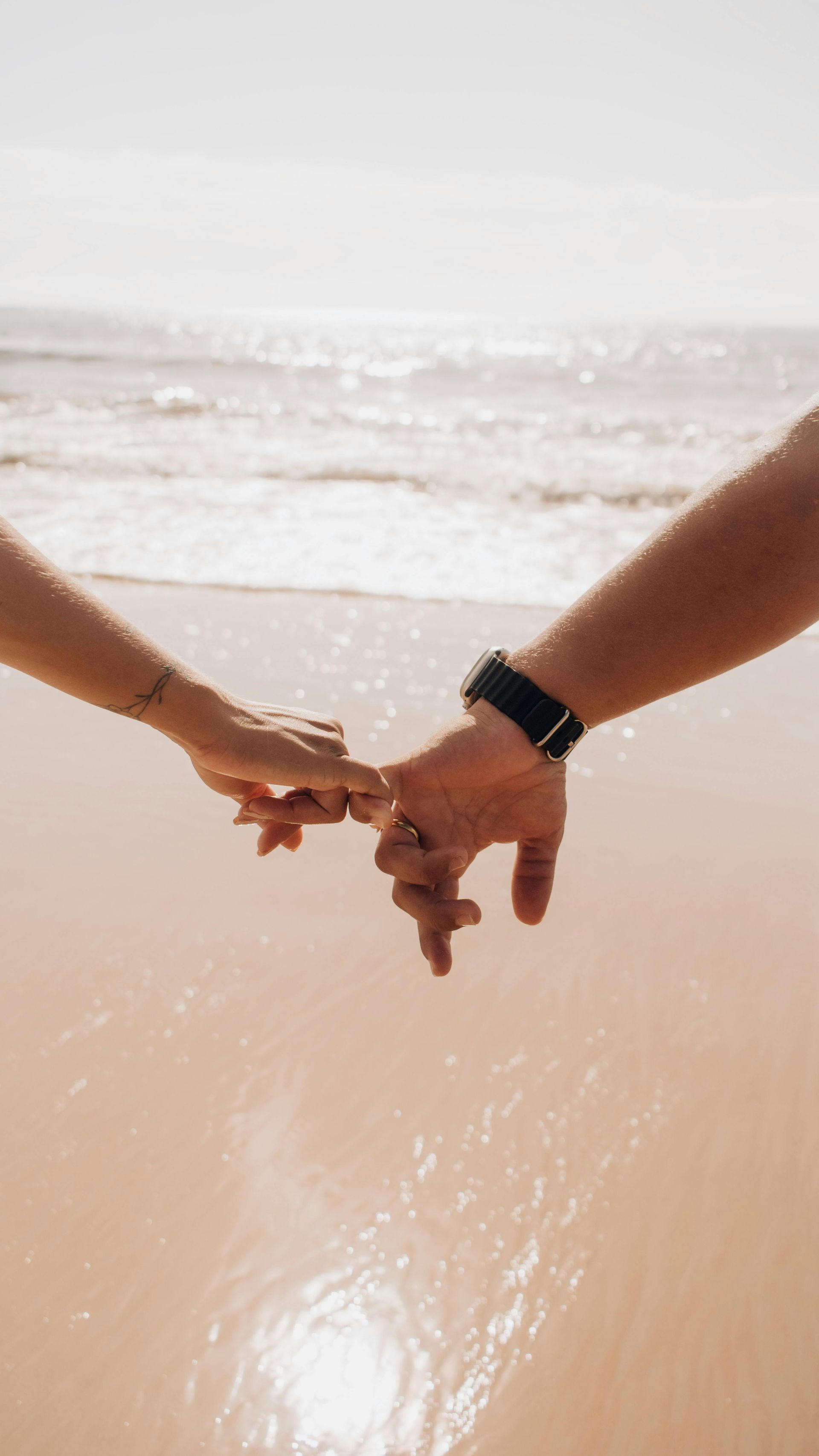 Due persone che si tengono per mano sulla spiaggia, con le onde dell'oceano sullo sfondo.