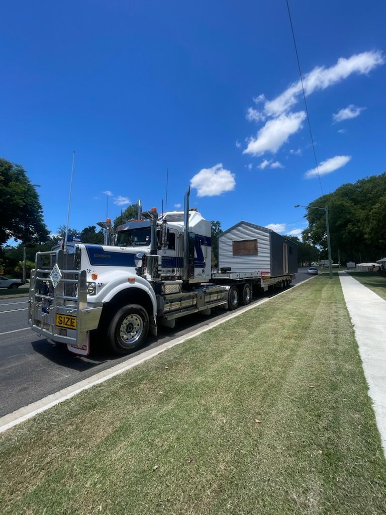 White semi-truck transporting a small shed on a trailer along a sunny road.— Supertilt Brisbane In Bracken Ridge, QLD