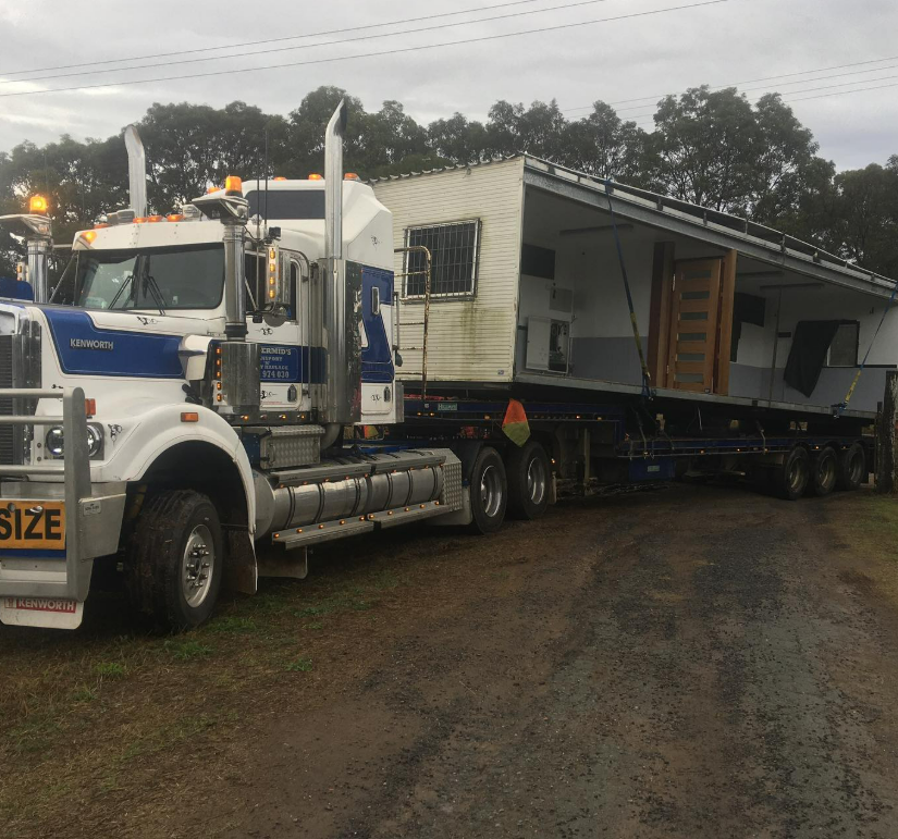 A White and Blue Semi-Truck Parked on a Dirt Lot, Hauling a Large House — Supertilt Brisbane In Bracken Ridge, QLD