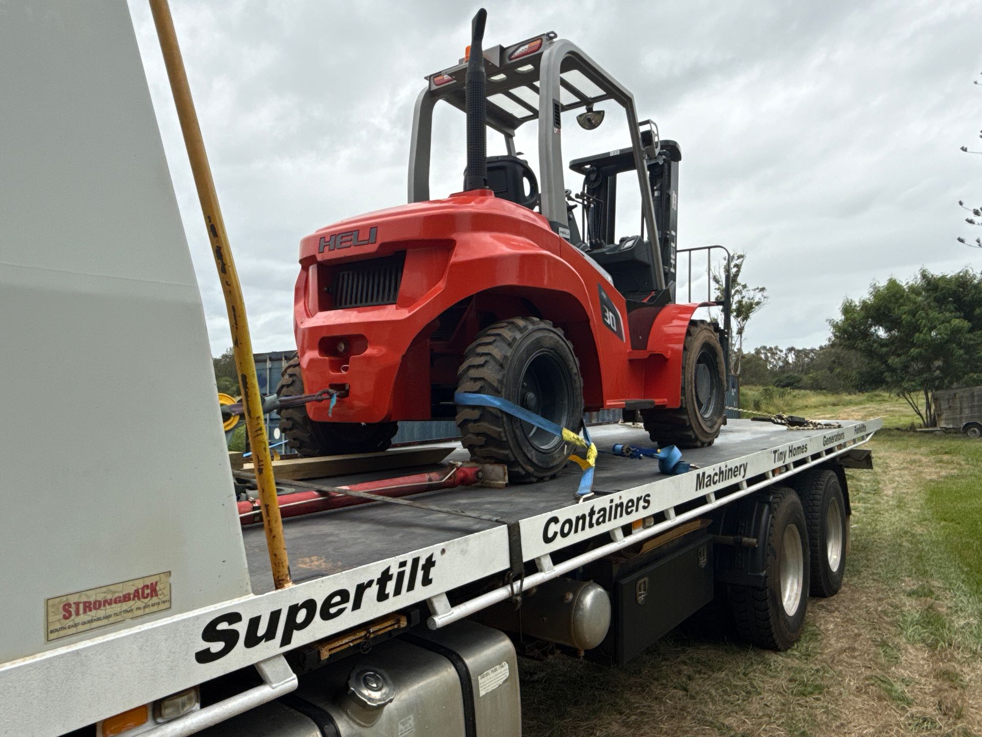 Orange forklift secured on a flatbed trailer labeled 