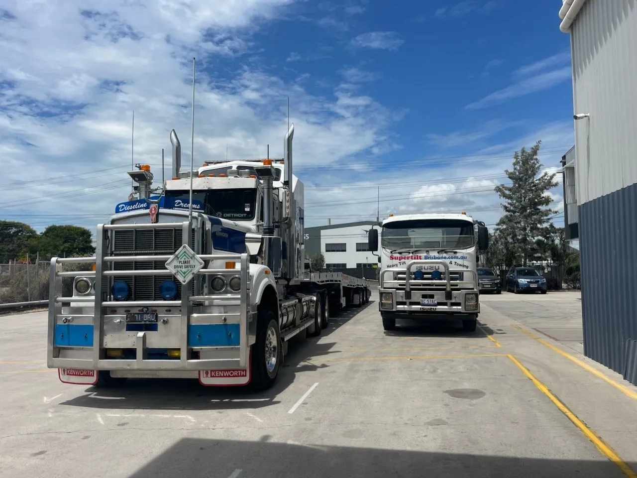 Two semi-trucks parked on a paved lot beside a building under a partly cloudy sky — Supertilt Brisbane In Pinkenba, QLD