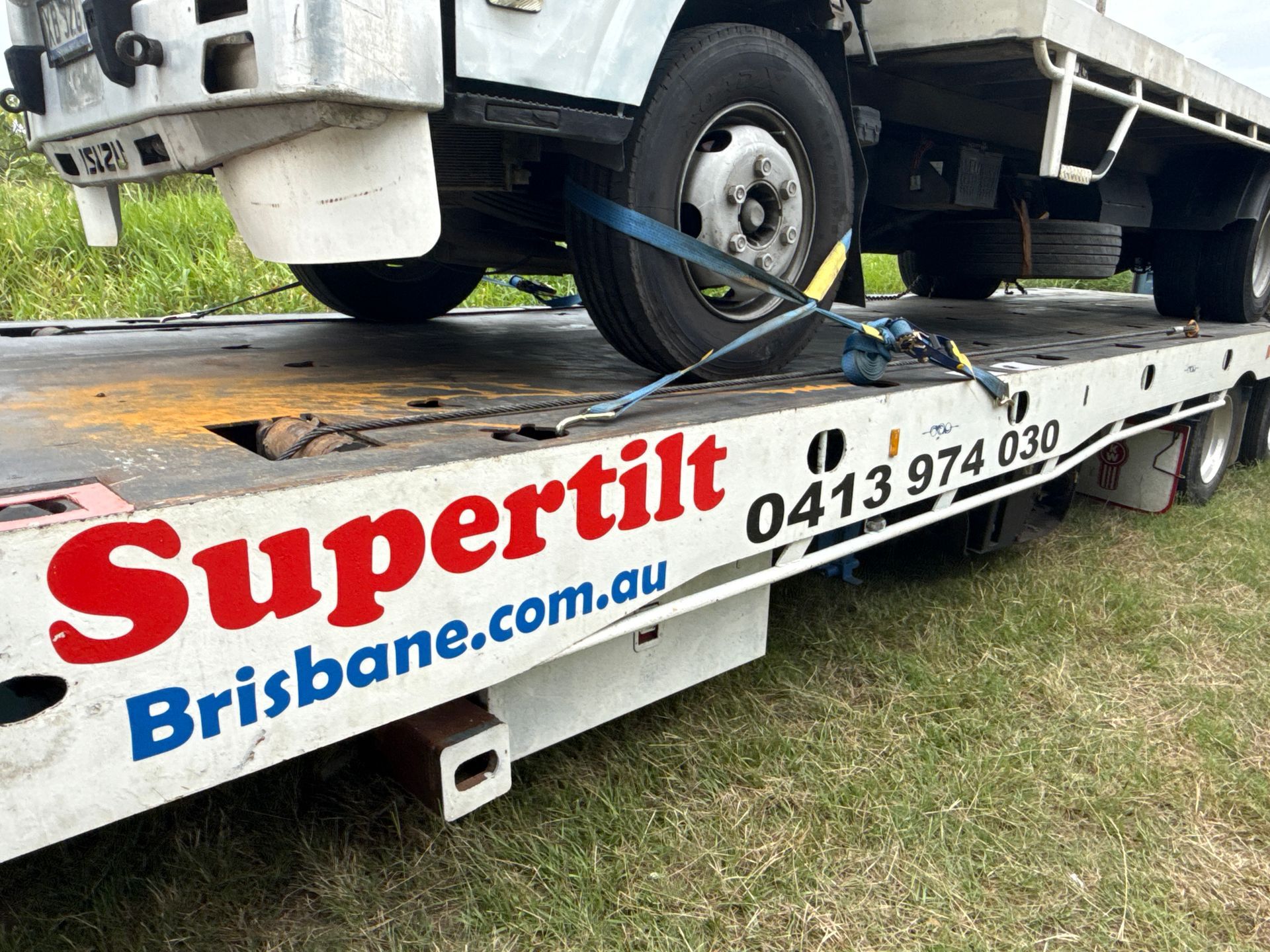 A white truck secured to a Supertilt Brisbane flatbed tow truck with straps — Supertilt Brisbane In North Lakes, QLD