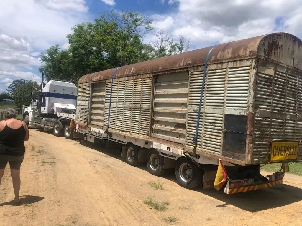 Semi-truck hauling an old, weathered livestock trailer on a dirt road; a person stands nearby — Supertilt Brisbane In Bracken Ridge, QLD