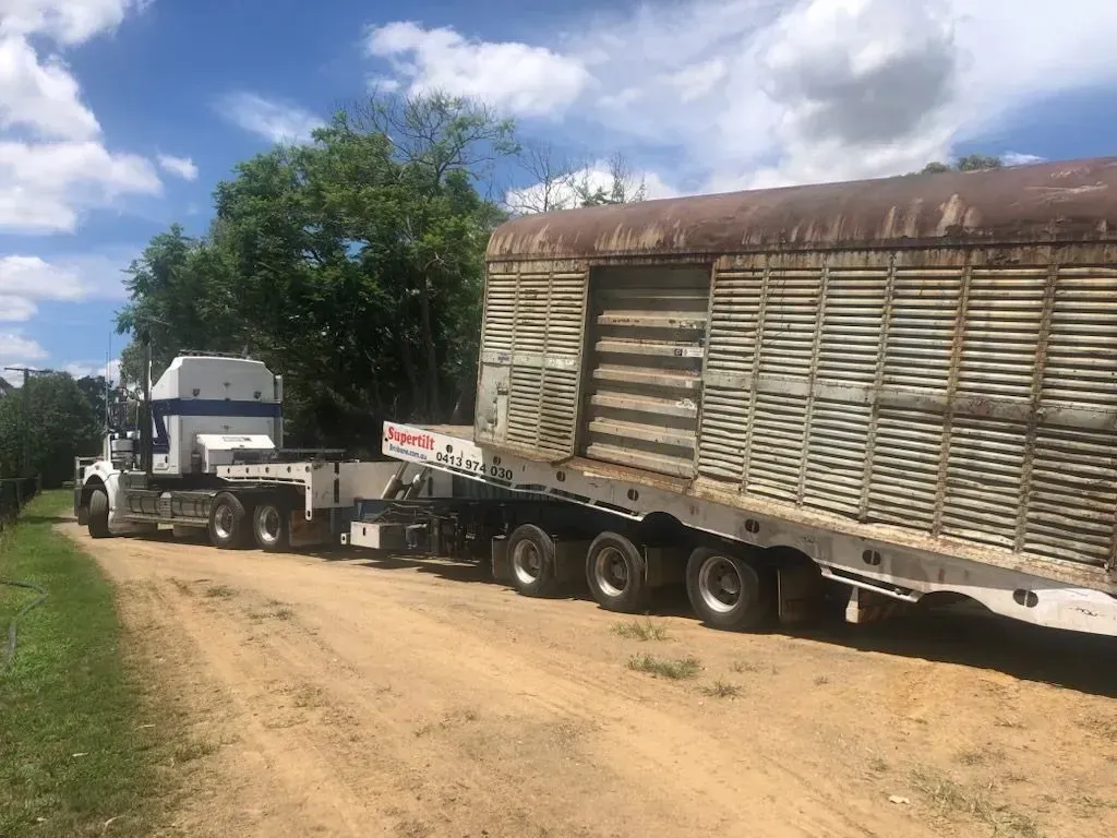 Truck with a large, weathered, rectangular trailer on a dirt road, trees in the background, blue sky — Supertilt Brisbane In Bracken Ridge, QLD