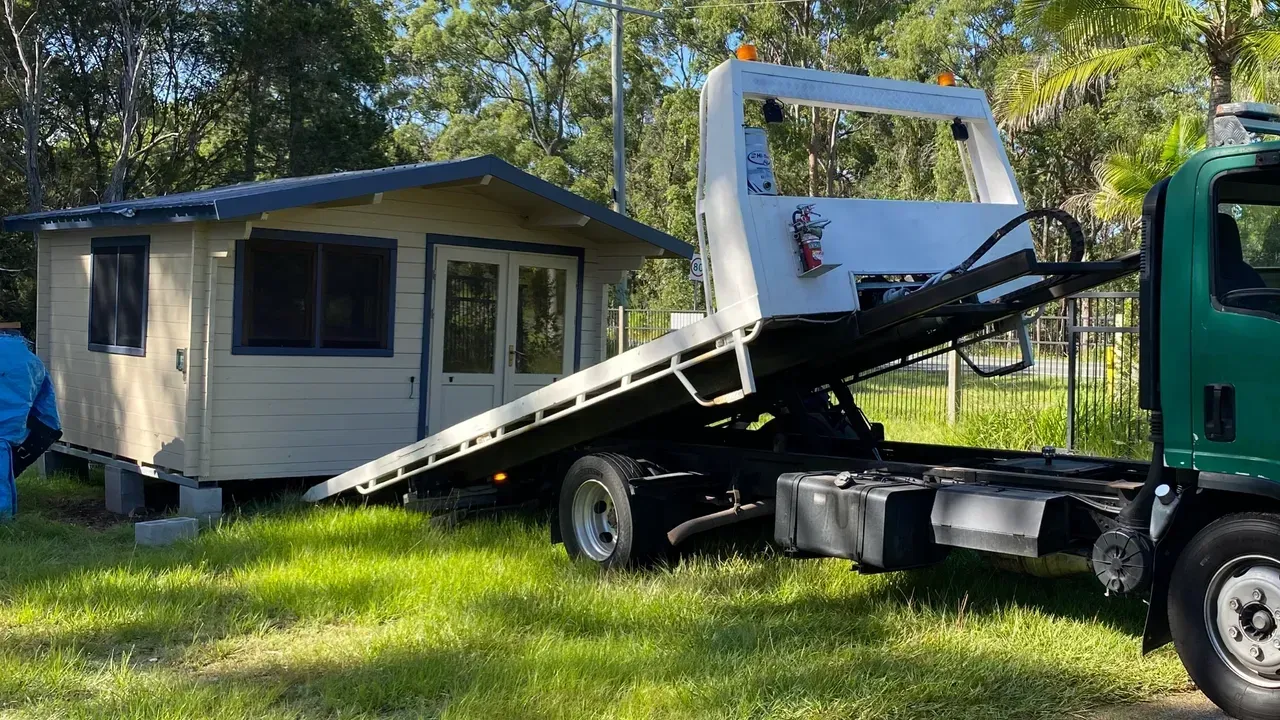 A Small Wooden Building is Being Loaded Onto a Flatbed Tow Truck — Supertilt Brisbane In Pinkenba, QLD