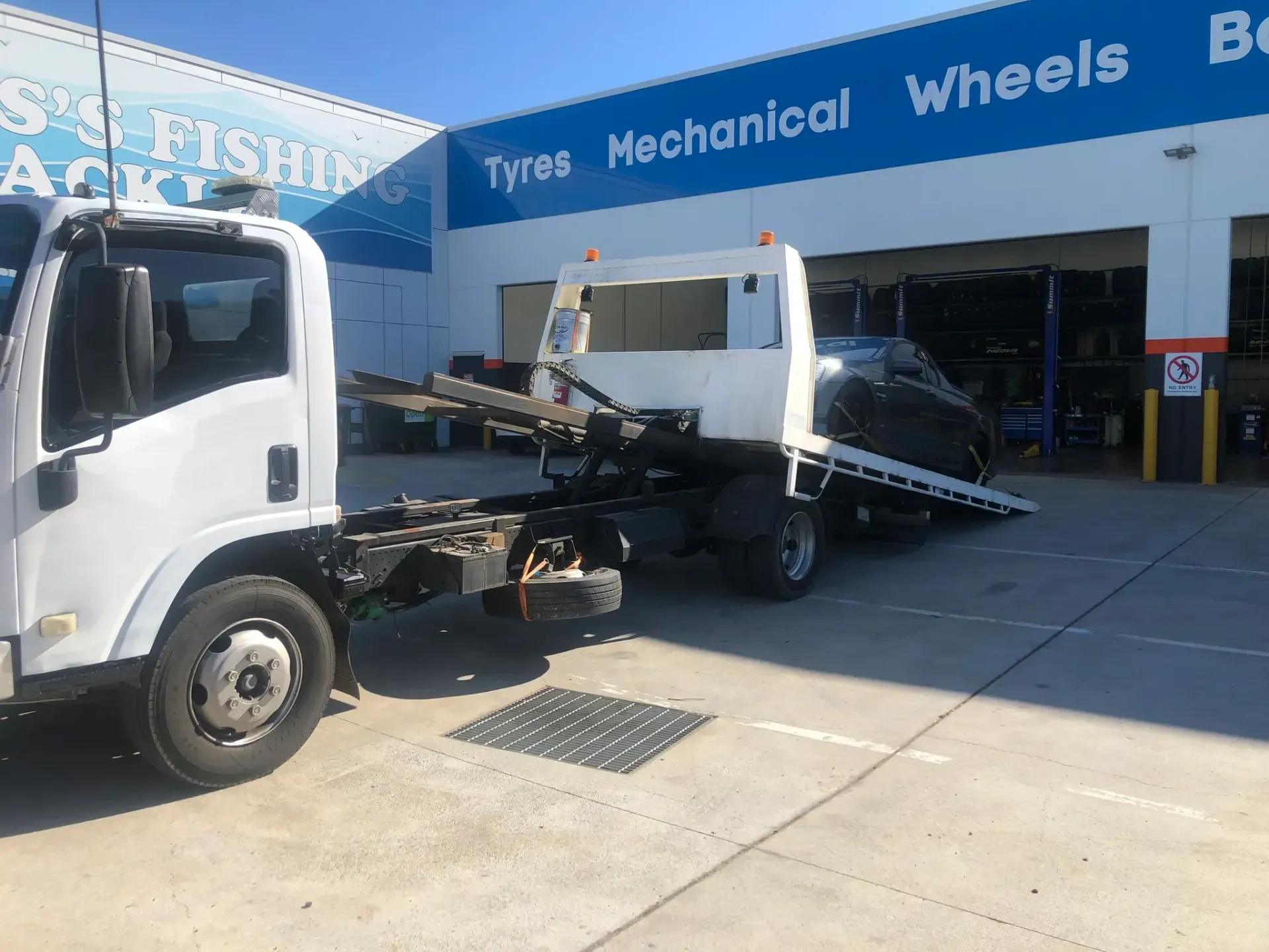 White Tow Truck Loading a Black Car in Front of a Shop With Blue Signage — Supertilt Brisbane In Acacia Ridge, QLD